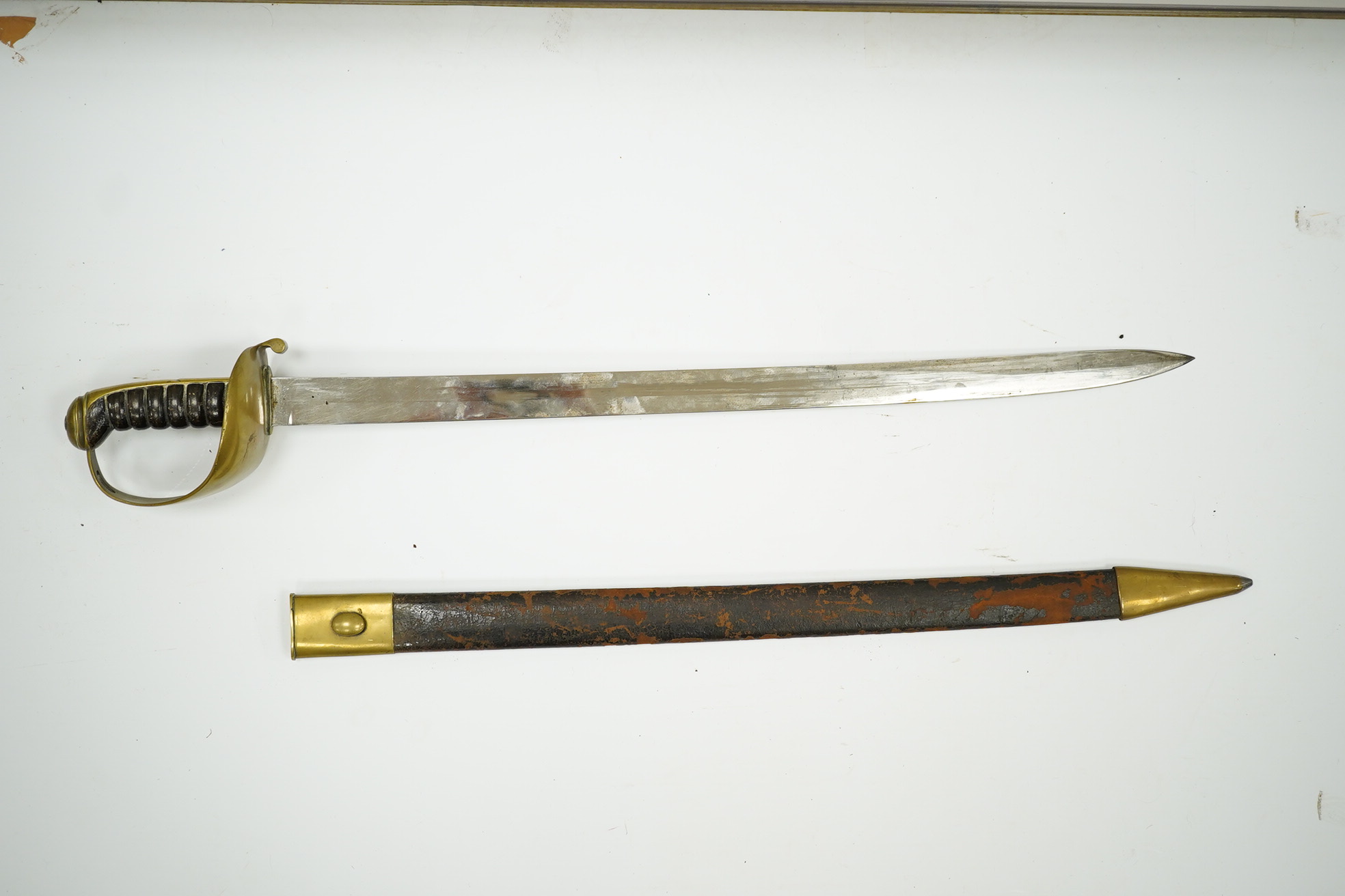 A late 19th century boarding cutlass with plain blade, plain brass guards and mounts, and leather covered grip, in its brass mounted leather scabbard (the chape is an associated replacement). Condition - fair